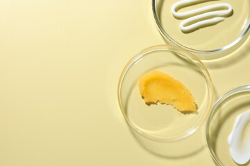 Different cosmetic products in Petri dishes on pale yellow background, flat lay. Space for text