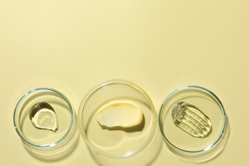 Different cosmetic products in Petri dishes on pale yellow background, flat lay. Space for text