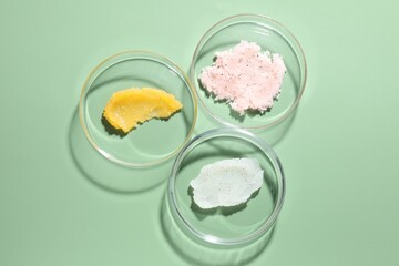 Different cosmetic products in Petri dishes on green background, flat lay