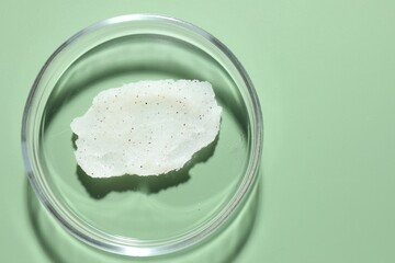 Cosmetic product in Petri dish on green background, top view. Space for text