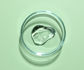 Cosmetic product in Petri dish on green background, top view