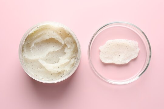 Natural scrub in Petri dish and jar of cosmetic product on pink background, flat lay