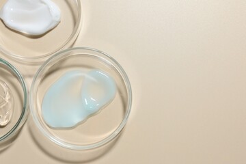 Different cosmetic products in Petri dishes on beige background, flat lay. Space for text