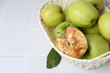 Spoiled apple and good ones in basket on white table, closeup. Space for text