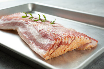 A closeup view of a stack of raw bacon on a baking sheet.
