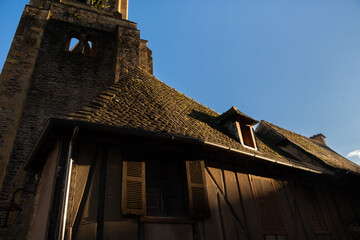 The golden light of sunset beautifully and softly illuminates, creating evocative shadows, an old medieval house and an ancient stone tower of the Abbey of Sainte-Foy under a clear blue sky in Conques