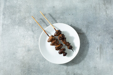 A top down view of some skewers of BBQ chicken heart, on a plate.
