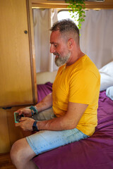 Mature man enjoying mobile gaming inside his cozy camper van, embracing leisure and travel on a sunny weekend getaway