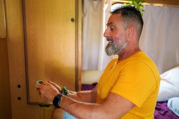 Middle aged man playing mobile game while relaxing inside compact campervan interior