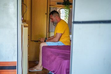 Middle aged man enjoying mobile gaming on his smartphone while relaxing inside his camper during a summer vacation getaway