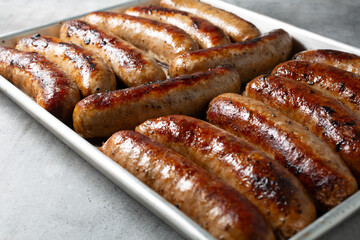 A closeup view of several cooked Italian sausages, on a baking sheet.
