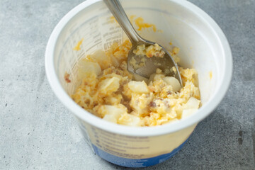 A view of spoon inside a package cup of instant breakfast bowl.