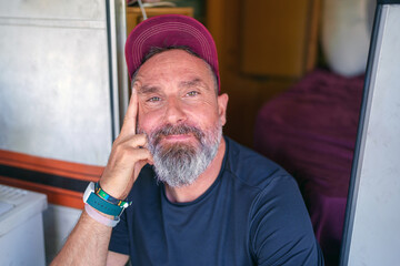 Mature traveler with beard resting on camper doorstep, wearing baseball cap, relaxing during road trip journey