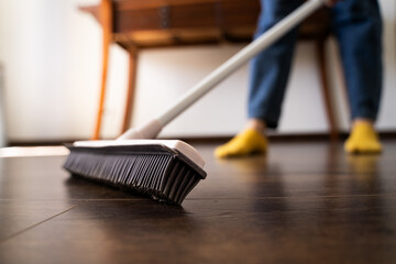 Close-up of woman sweeping dust from the wooden floor with a rubber mop in living room at home,...