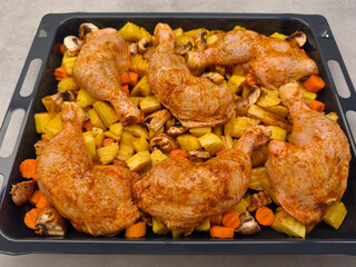 Raw chicken legs with potatoes, carrots, and mushrooms seasoned and ready for baking