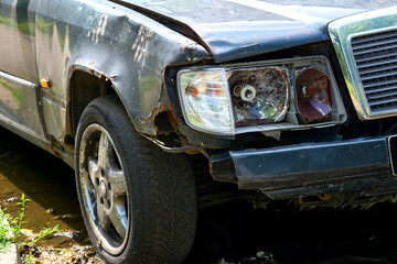 Old car with a rusty wing, a broken headlight and a flat tire