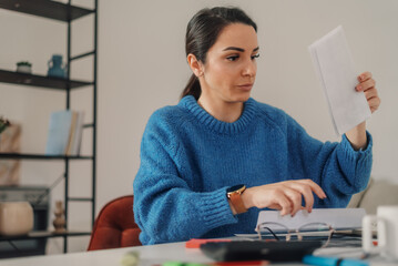Woman managing home finances and reading documents at home office desk