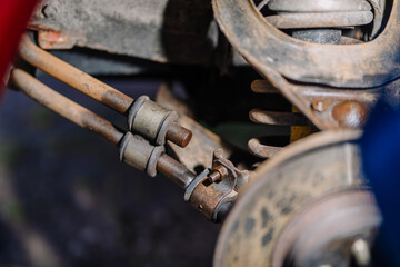Close-up of a rusty vehicle suspension system showing metal rods, bushings, coil spring, and mounting components in detail during maintenance.