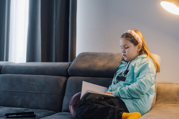 Young girl reading a book on the sofa in living room