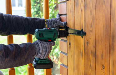 A worker in gloves uses a cordless screwdriver in the household. Cordless drill-screwdriver....