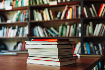 Books on table with library shelves visible on the background. Some volumes on a table in front of blurred rows of books