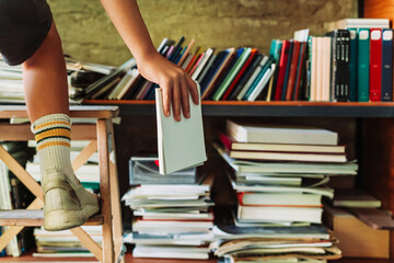 Boy placing a book on a high shelf using a small stool in a library setting. Learning and...