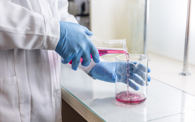 Scientist or medical in lab coat holding test tube with reagent, mixing reagents in glass flask in...