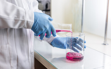 Scientist or medical in lab coat holding test tube with reagent, mixing reagents in glass flask in...