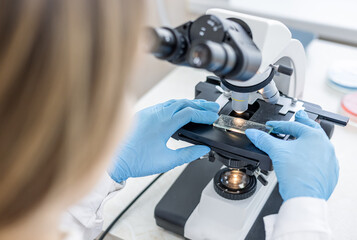 Female scientist using microscope in laboratory. Biotechnology specialist looking under microscope,...