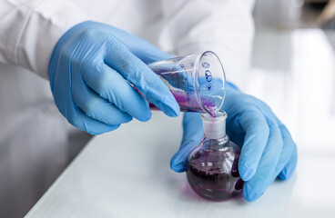 Hispanic woman scientist analyzing blue chemical in laboratory wearing lab coat and safety glasses