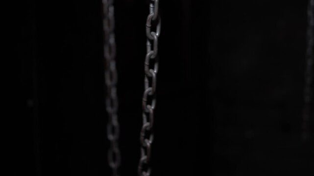 Close-up of hanging chains in the dark on a black background. The chains swing from side to side. 