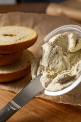 A view of a butter knife scooping up some dairy-free cream cheese, next to slices of gluten-free bagels.
