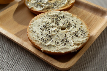 A view of a gluten-free bagel, featuring toppings as diary-free cream cheese and poppy seeds.