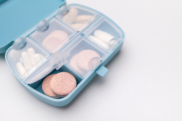 Blue pill organizer, pillbox with different vitamins, capsules, tablets, pills, dietary supplements on gray background flat lay top view. Medical pharmaceutical concept, health and beauty