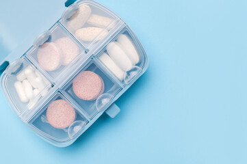 Blue pill organizer, pillbox with different vitamins, capsules, tablets, pills, dietary supplements on blue background flat lay top view. Medical pharmaceutical concept, health and beauty