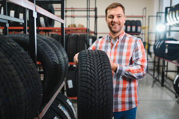 Smart male customer choosing new tires in the supermarket for buying. Big shopping mall with car...