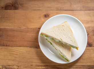 Sandwich with fresh vegetables and creamy salad dressing on white plate  on wooden background