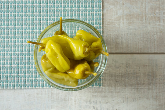 A top down view of several pickled pepperoncini peppers in a small glass bowl.