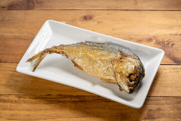 Top view of crispy fried mackerel on a white  plate placed on a natural wooden surface. Thai cuisine presentation perfect for menu or cooking content.