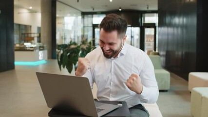 Caucasian bearded businessman working on laptop shocked by sudden victory, game winning lottery goal achievement, good career news. Excited guy freelancer clenching fists sitting in modern hotel lobby - Powered by Adobe