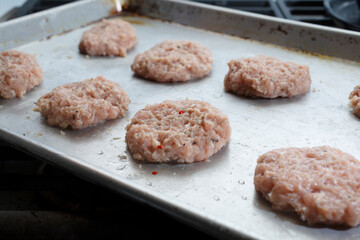 A view of a baking tray of raw chicken sausage patties.