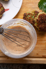 A top down view of a whisk in a plastic container, stirring a sauce for some crabcakes.