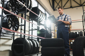 Portrait man mechanic holding new tyre on background store, car tire service concept