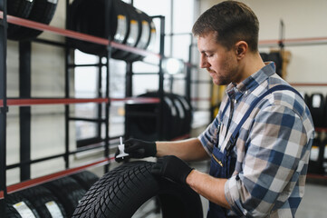 worker tire fitting in the car service, auto mechanic checks the tire and rubber tread for safety, concept: repair of machines, fault diagnosis, repair. man buy in car service shop
