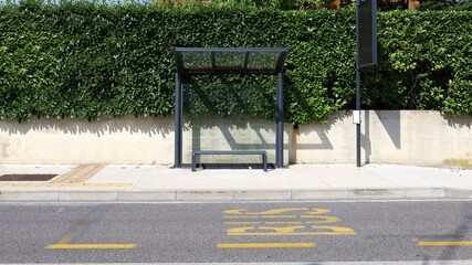 Bus shelter and bus stop pole at the roadside. Hedge on behind, street in front. Background for copy space.