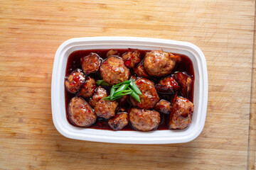 A top down view of a white plastic container of grape jelly meatballs.