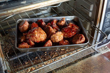 A view of a tray of grape jelly meatballs inside a convection oven.