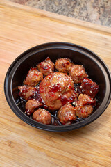 A view of different sized grape jelly meatballs in a black plastic container.