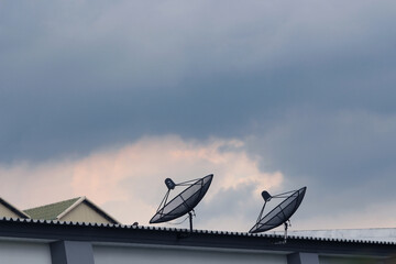 Satellite Dishes Against Cloudy Sky: A duo of satellite dishes stands sentinel atop a building, their parabolic forms contrasting with the dramatic backdrop of a cloudy sky.