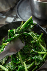 A view of a pair of tongs grabbing a pile of wilted kohlrabi greens.